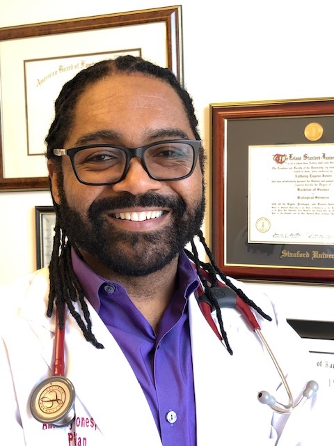 Dr. Anthony Jones, MD smiling in his office with framed diplomas