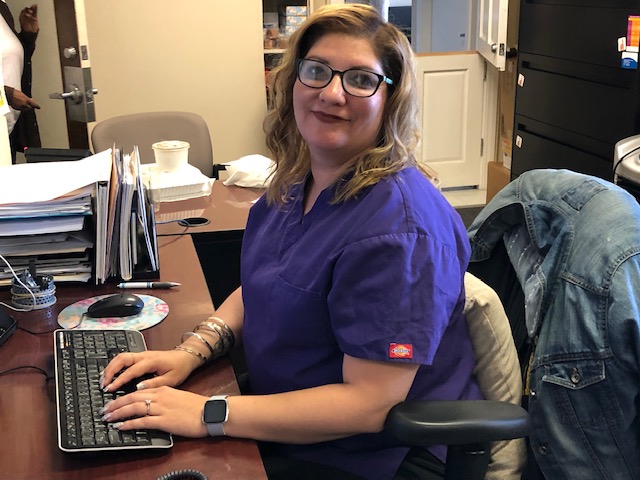 Staff member in purple scrubs working at the front desk computer